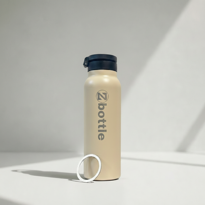 Botella beige con tapón negro y grabado metálico, sin aro negro superior, sobre fondo fotográfico blanco